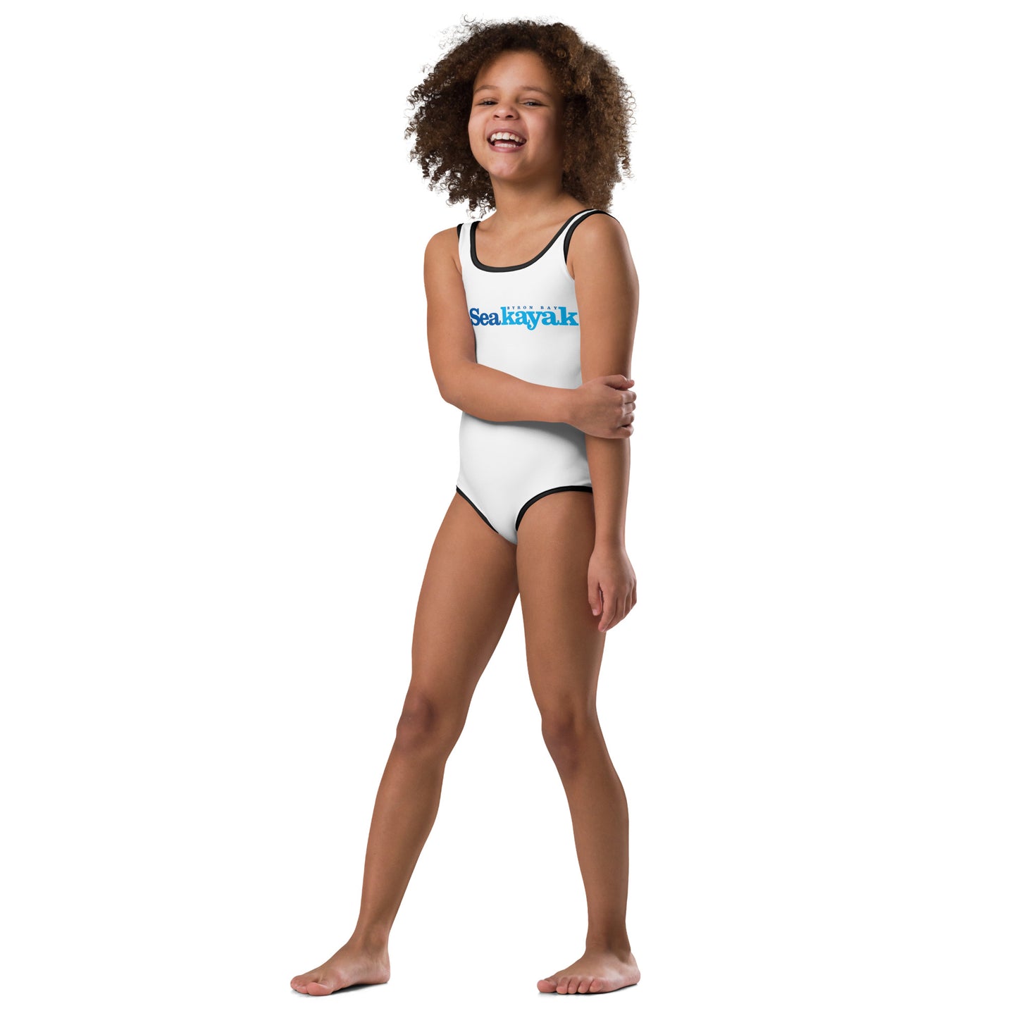  Girls One-Piece Swimsuit - White with black trim/detail - Back view of the swimsuit on a girl standing with one arm crossed in front - With Go Sea Kayak Byron Bay logo on front - Genuine Byron Bay Merchandise | Produced by Go Sea Kayak Byron Bay 