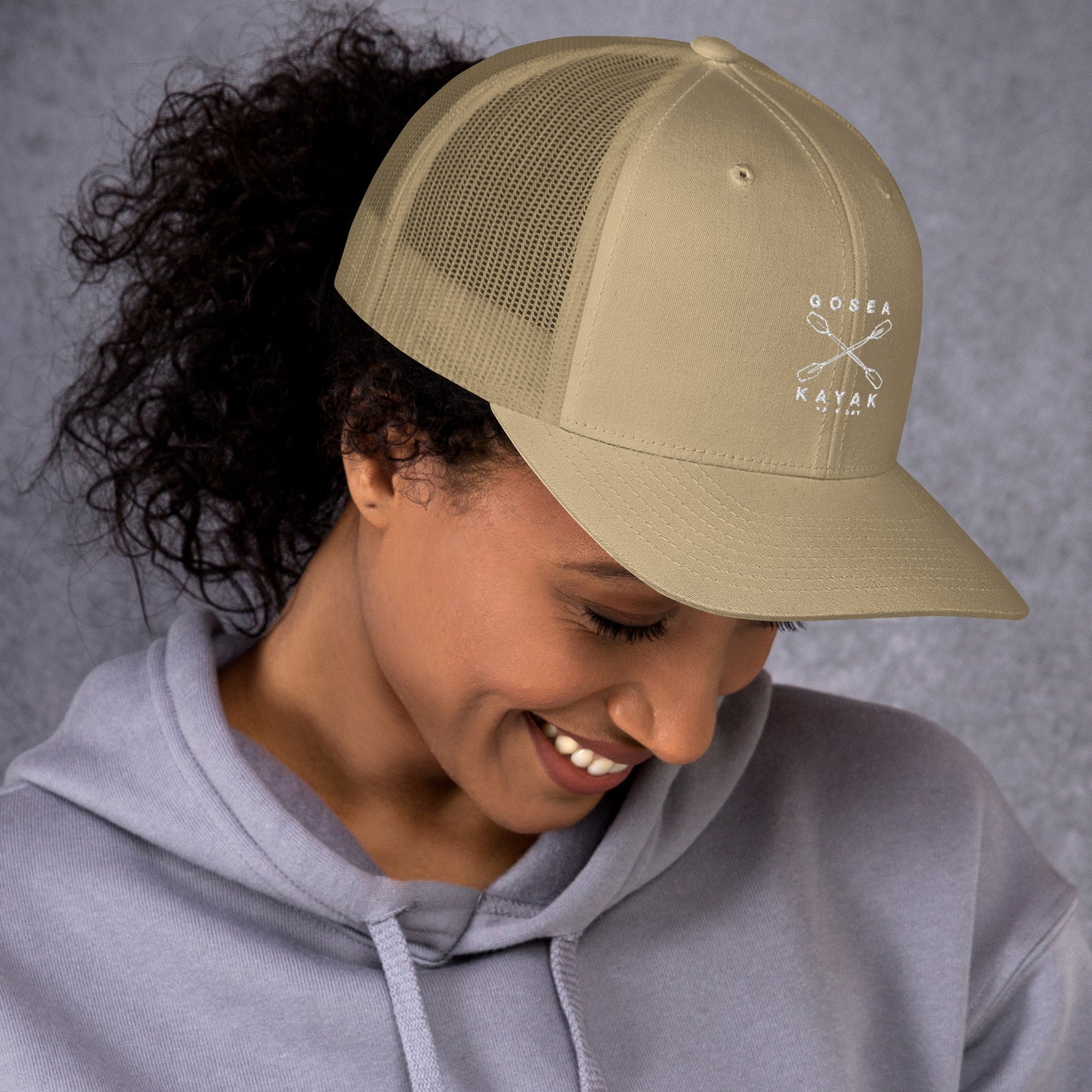  Trucker Cap - Khaki - side view - being warn by woman with her head down - Crossed Paddles Go Sea Kayak Crew logo in white on front - Genuine Byron Bay Merchandise | Produced by Go Sea Kayak Byron Bay 