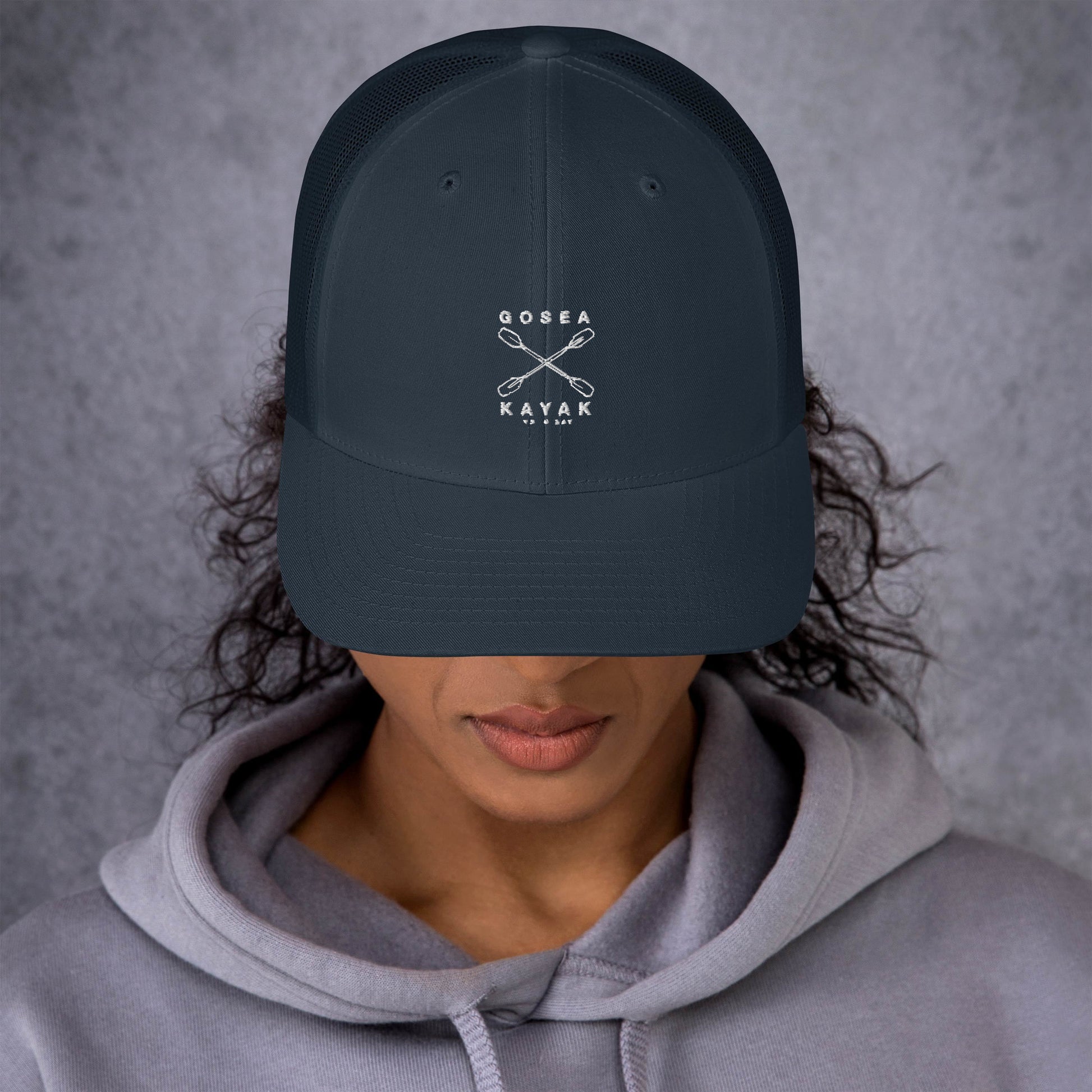  Trucker Cap - Navy - Front view - being warn by woman with her head down - Crossed Paddles Go Sea Kayak Crew logo in white on front - Genuine Byron Bay Merchandise | Produced by Go Sea Kayak Byron Bay 