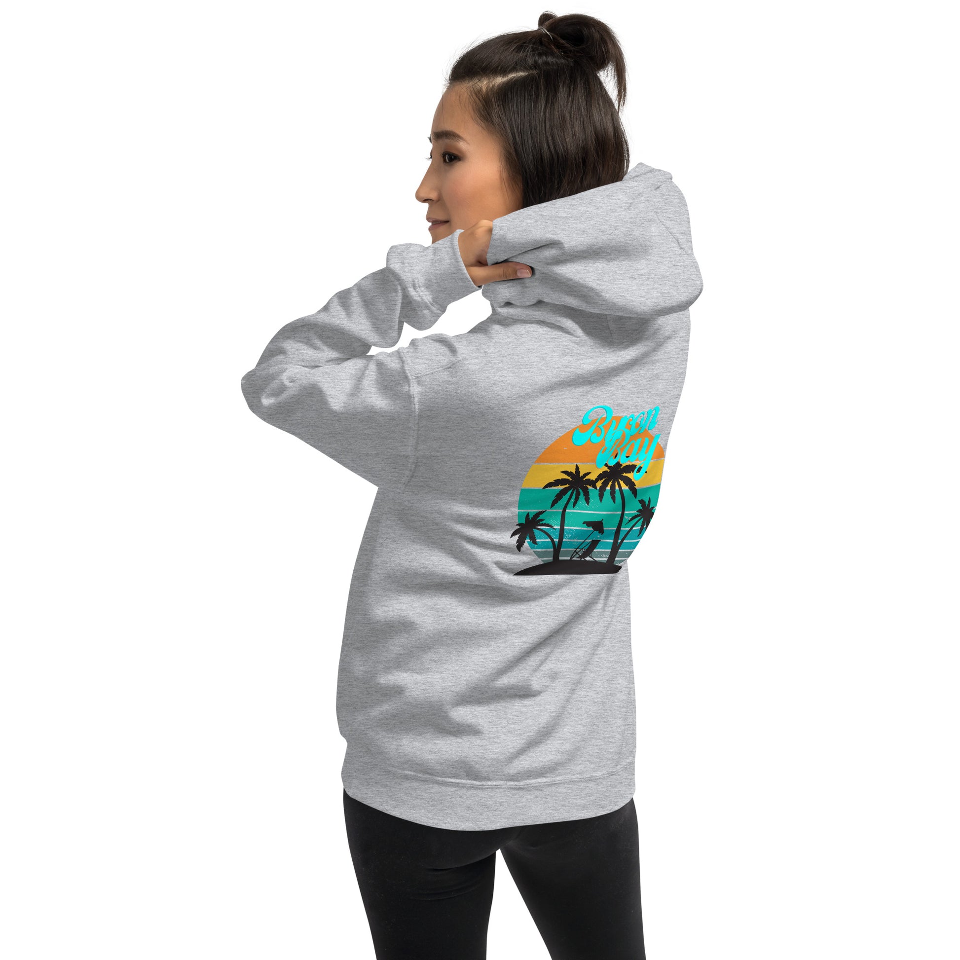  Unisex Hoodie - Sport Grey - Side back view being warn by woman pulling the hood on looking back over her shoulder - Byron Bay design on back, plain front with pouch pocket - Genuine Byron Bay Merchandise | Produced by Go Sea Kayak Byron Bay 