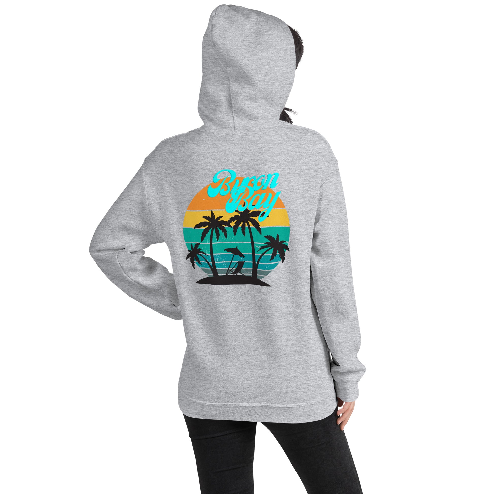 Unisex Hoodie - Sport Grey - back view being warn by woman with the hood on and one hand in the pocket - Byron Bay design on back, plain front with pouch pocket - Genuine Byron Bay Merchandise | Produced by Go Sea Kayak Byron Bay 