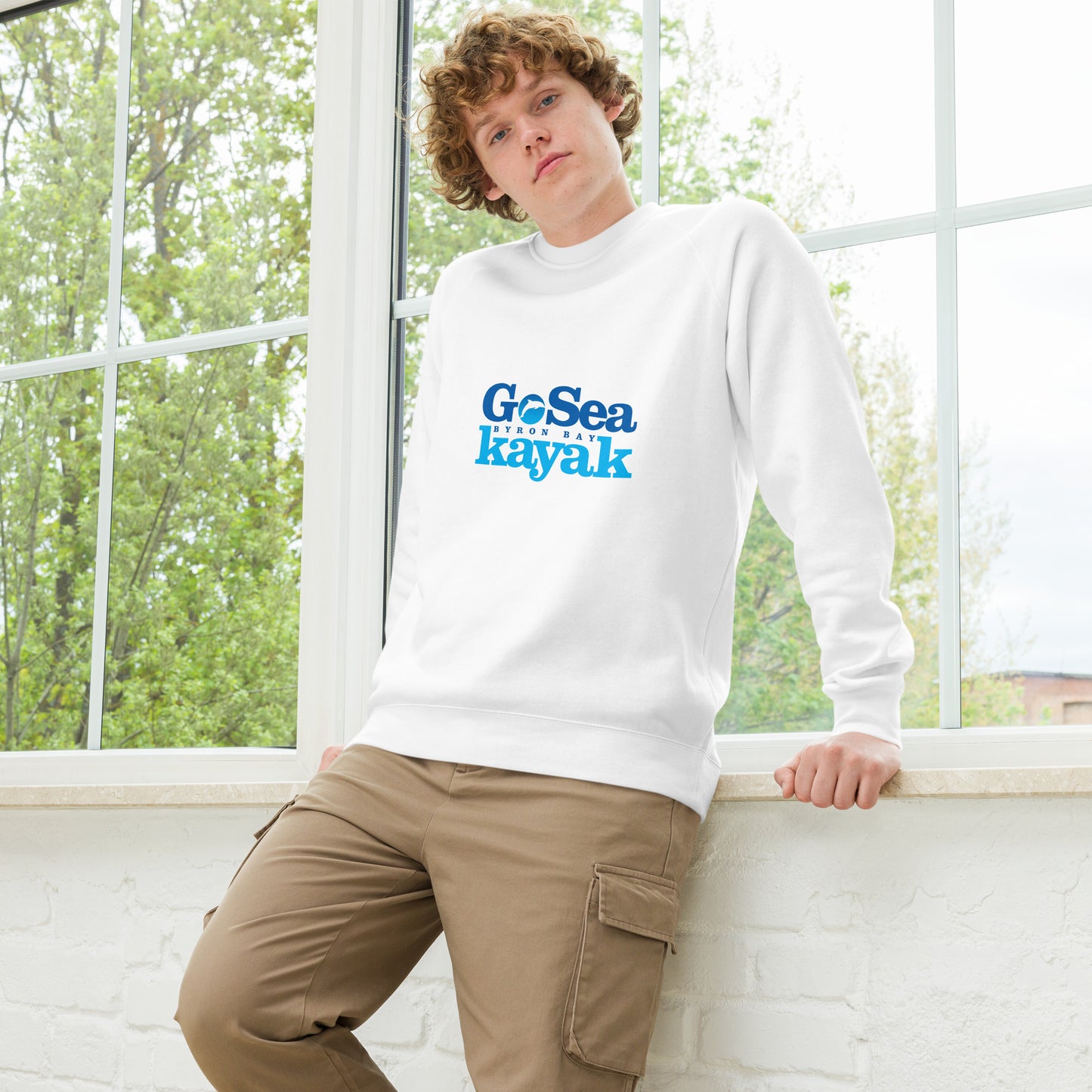  Unisex Sweatshirt - White - Front view being warn by man leaning on a window - Go Sea Kayak Byron Bay logo on front - Genuine Byron Bay Merchandise | Produced by Go Sea Kayak Byron Bay 