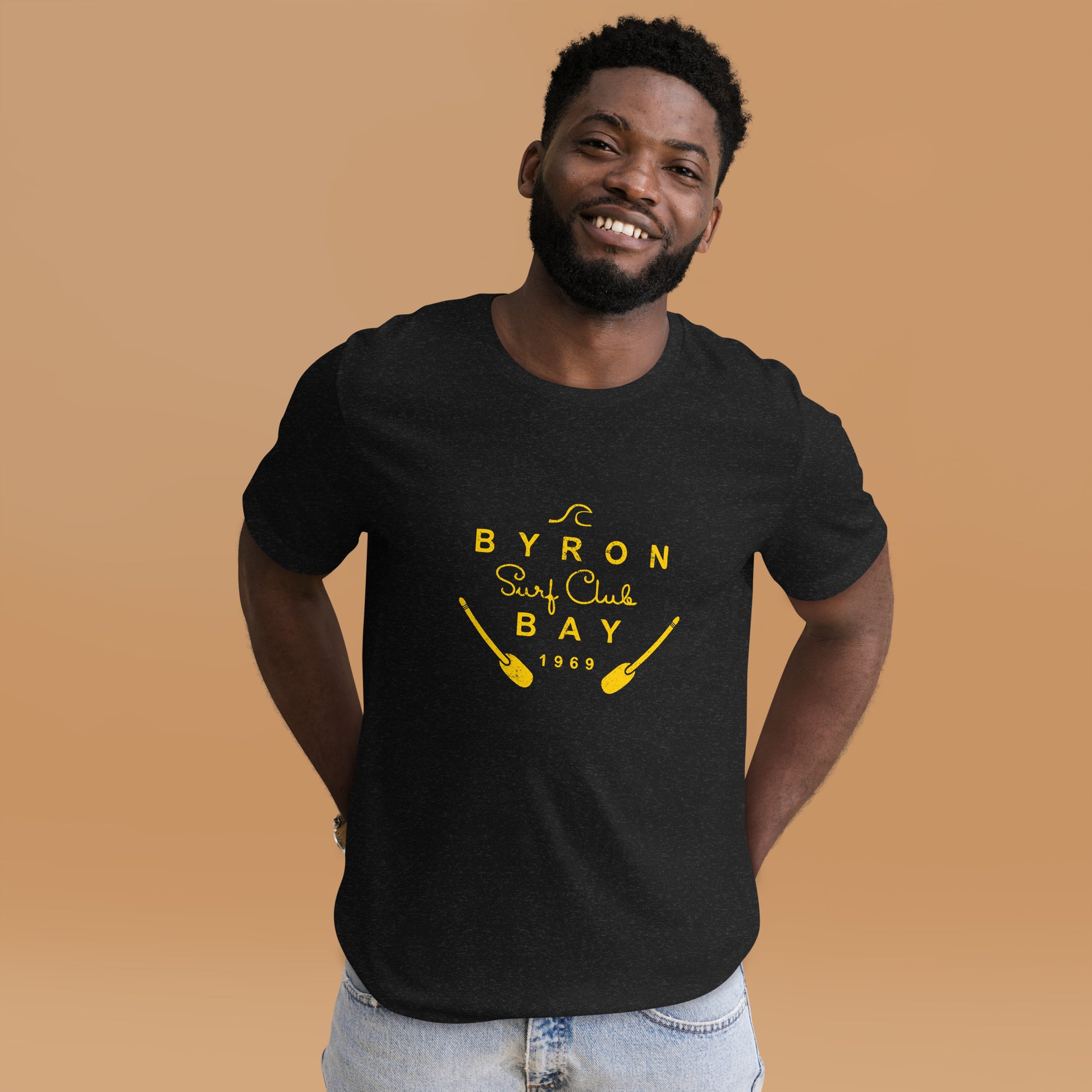  Unisex T-Shirt - Black Heather - Front view, man standing with both hands in back pockets - Byron Bay Surf Club logo on front - Genuine Byron Bay Merchandise | Produced by Go Sea Kayak Byron Bay 