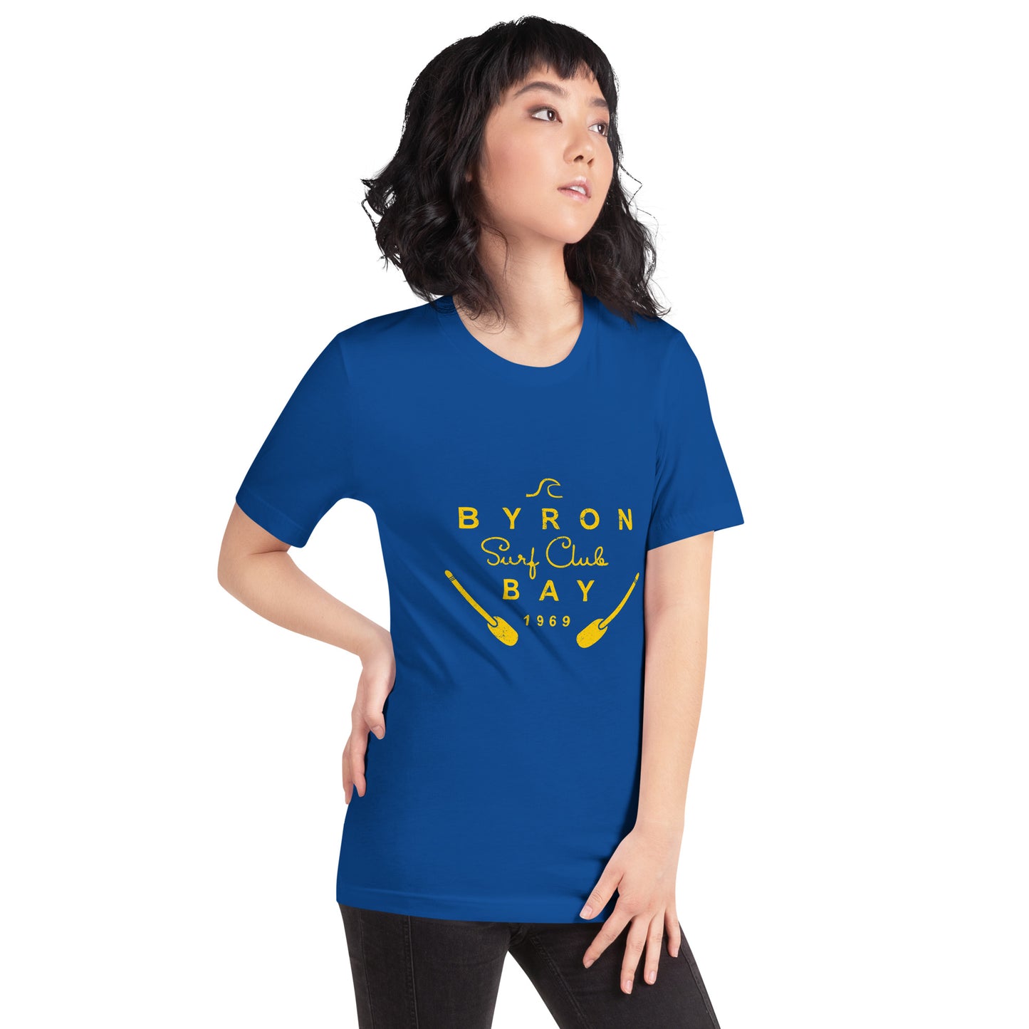  Unisex T-Shirt - True Royal Blue - Front view, on woman with on hand on hip - yellow Byron Bay Surf Club logo on front - Genuine Byron Bay Merchandise | Produced by Go Sea Kayak Byron Bay 