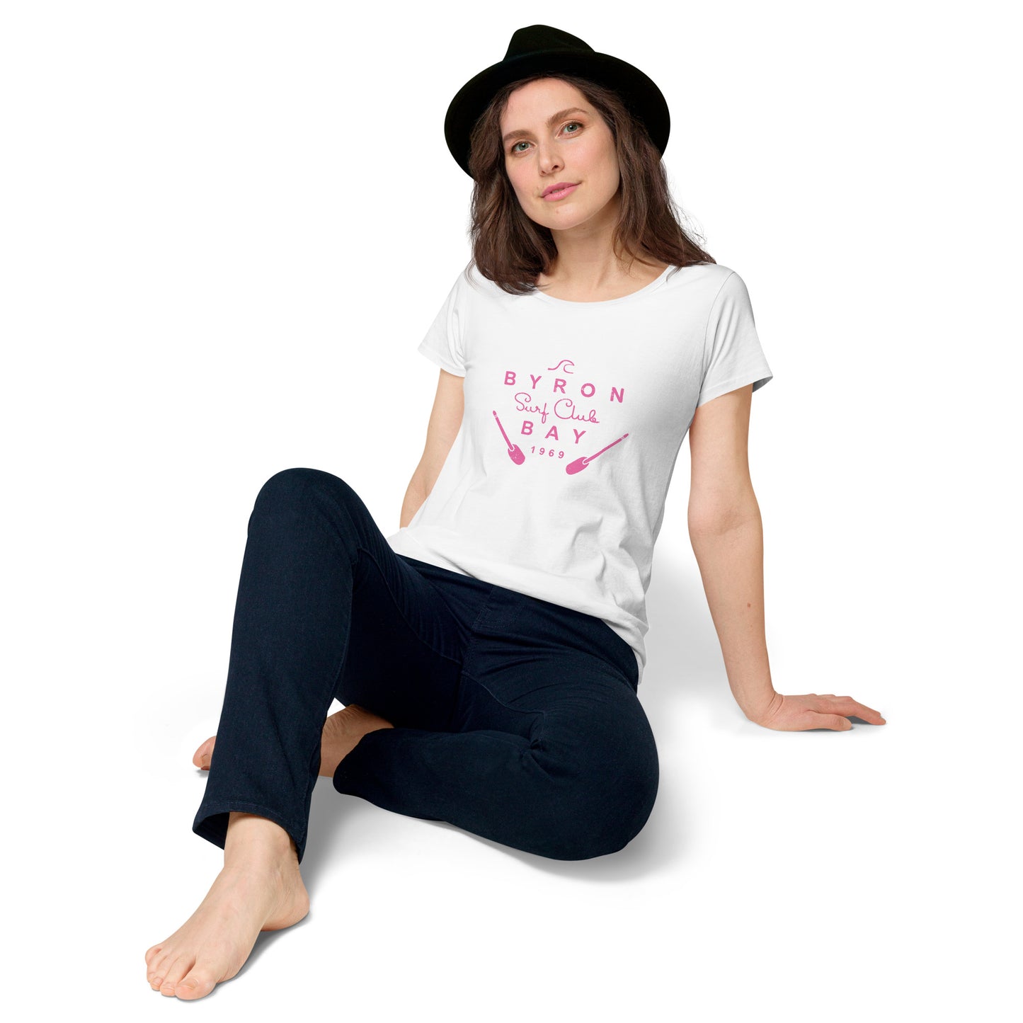  Women’s Round Neck Tee - White - Front view, woman on floor knee up resting back on her hands - pink Byron Bay Surf Club logo on front - Genuine Byron Bay Merchandise | Produced by Go Sea Kayak Byron Bay 