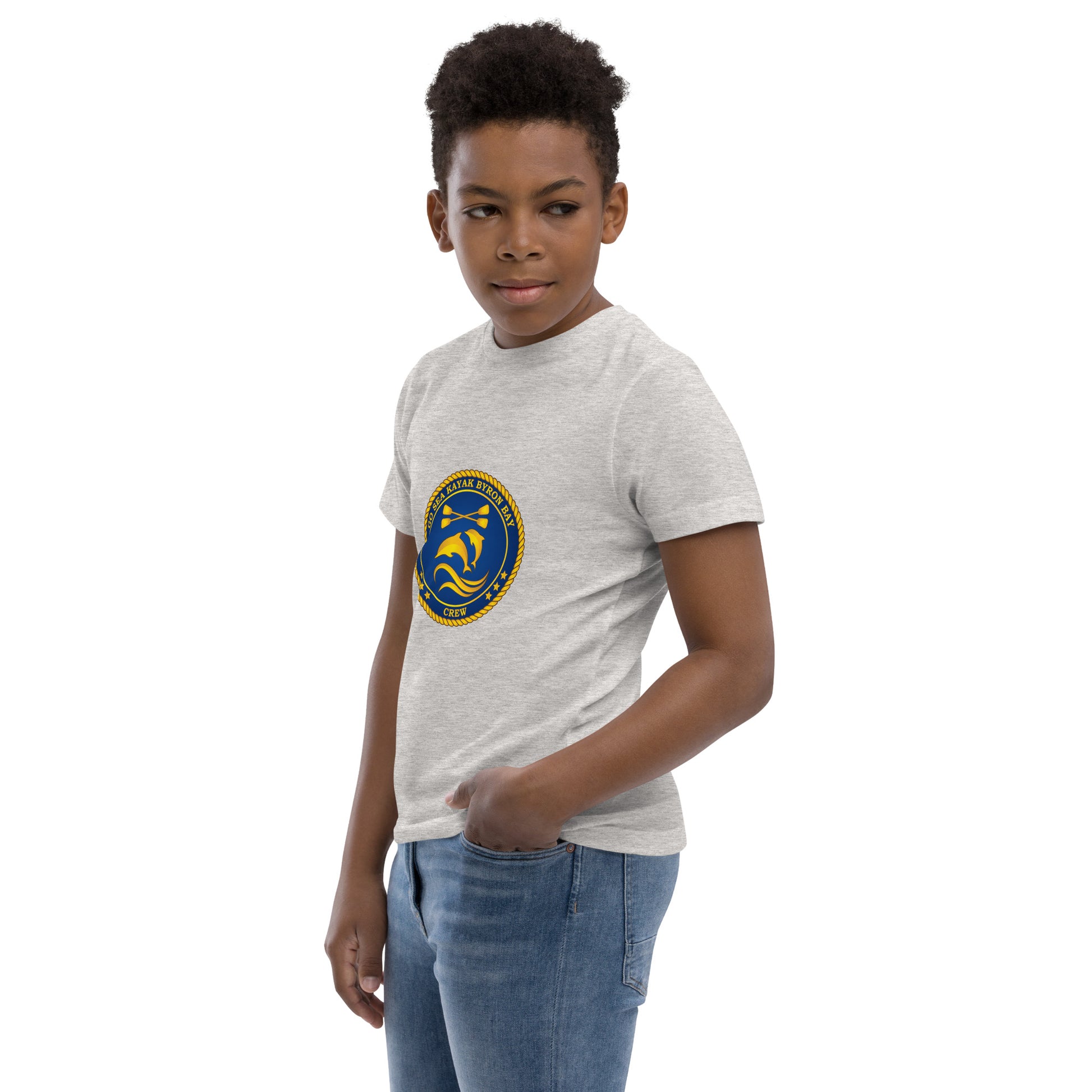  Kids T-Shirt - Natural / Heather colour - Side view, being warn on boy standing with a hand in his pocket - Go Sea Kayak Byron Bay Crew (issue 2018-2019) logo on front - Genuine Byron Bay Merchandise | Produced by Go Sea Kayak Byron Bay 
