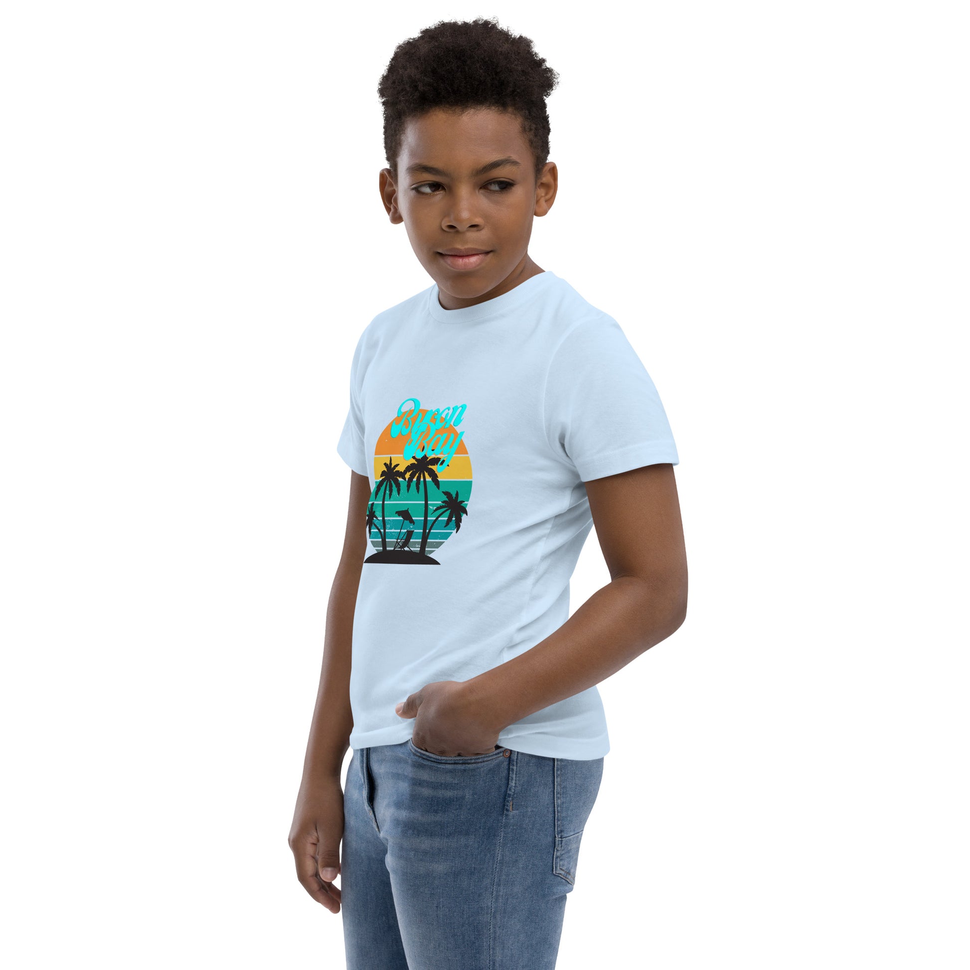  Kids T-Shirt - Light Blue - Side view, being warn on boy standing with a hand in his pocket - Byron Bay design on front - Genuine Byron Bay Merchandise | Produced by Go Sea Kayak Byron Bay 