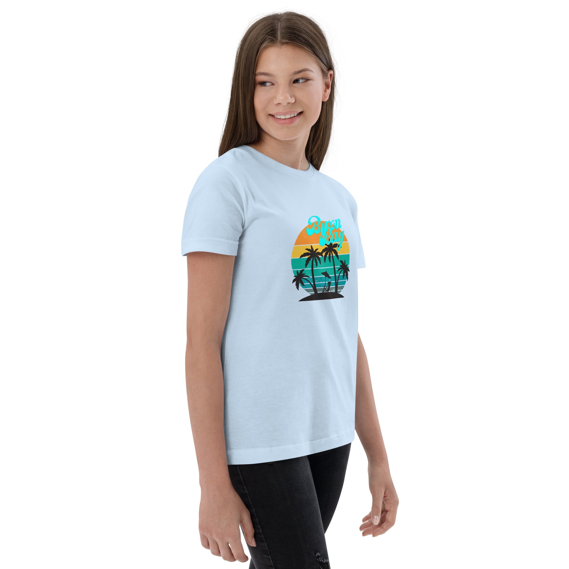  Kids T-Shirt - Light Blue - side view, being warn on a girl standing with her arms by her side - Byron Bay design on front - Genuine Byron Bay Merchandise | Produced by Go Sea Kayak Byron Bay 