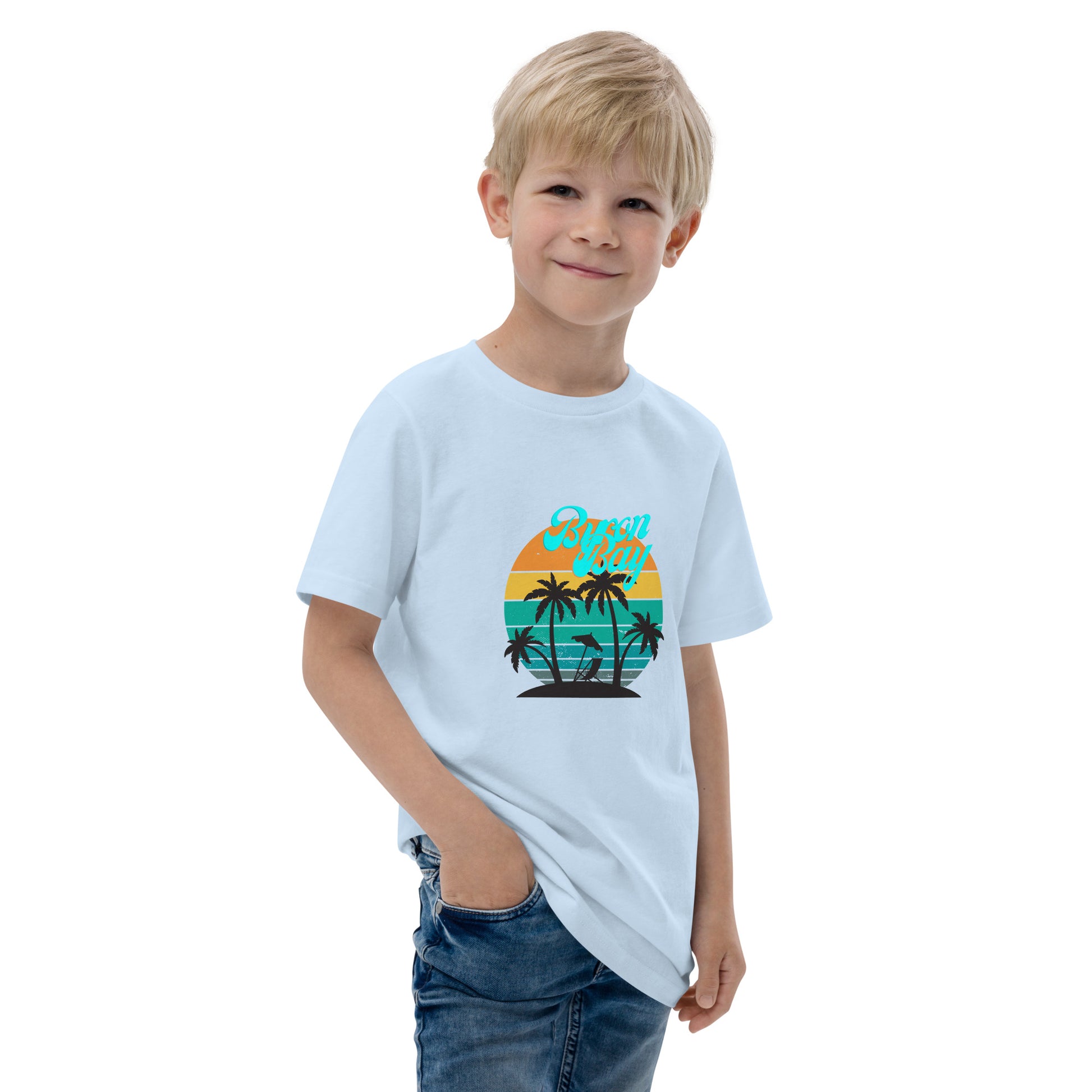  Kids T-Shirt - Light Blue - Front view, being warn on boy standing with a hand in his pocket - Byron Bay design on front - Genuine Byron Bay Merchandise | Produced by Go Sea Kayak Byron Bay 
